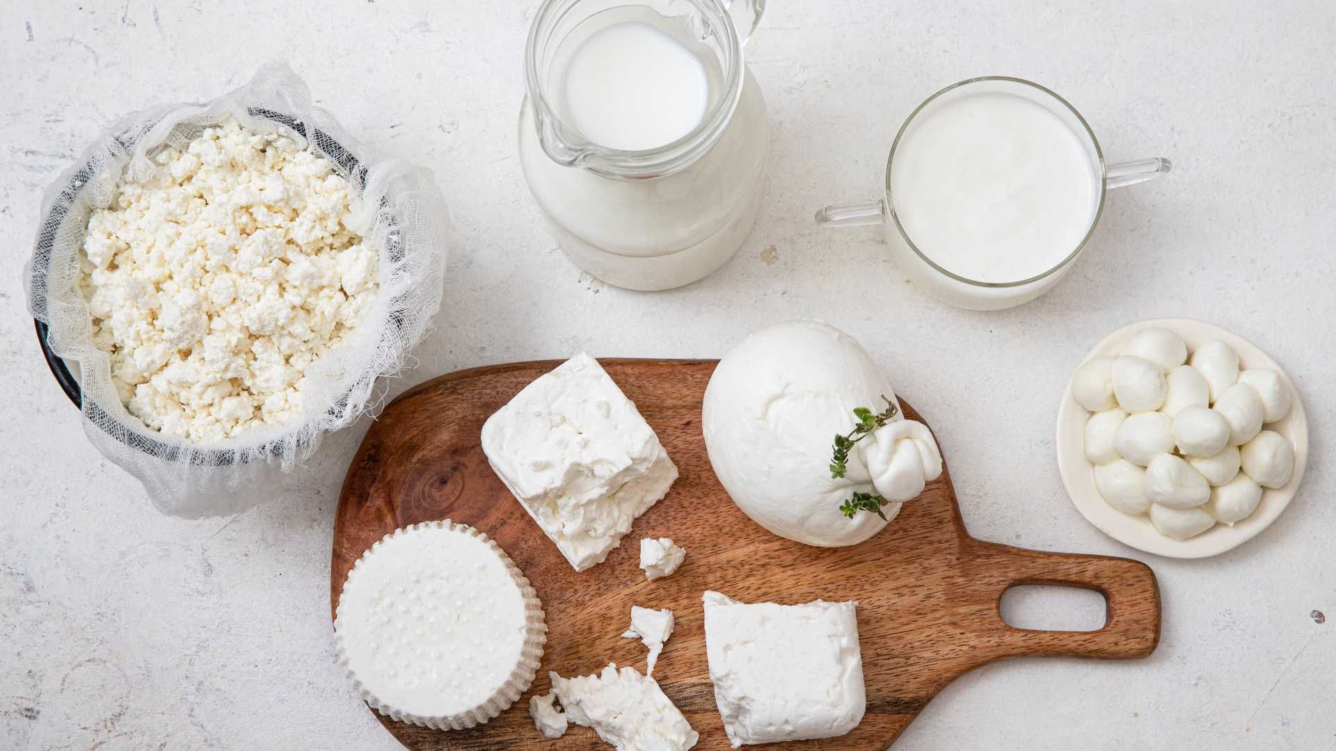 A wooden cutting board topped with various types of cheese and milk.