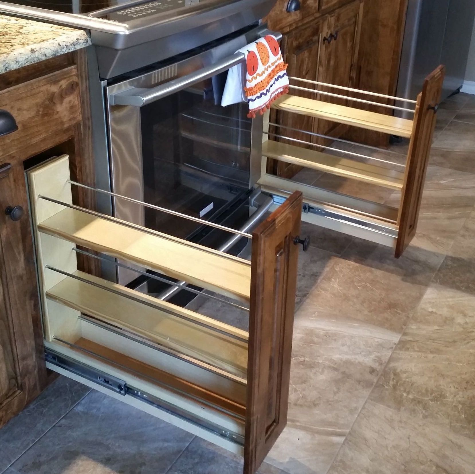 Pull-out spice racks beside oven in a brown kitchen.