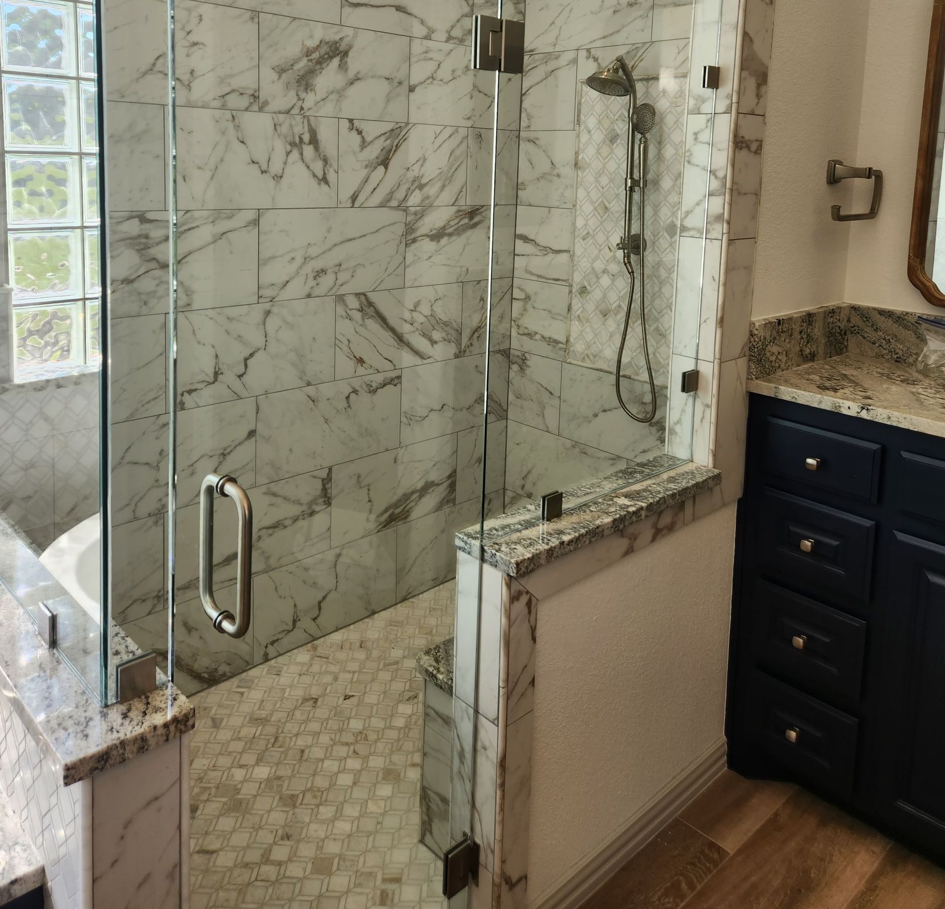 Walk-in shower with glass doors and marble tile walls, next to a navy blue vanity.