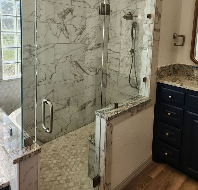 Walk-in shower with glass doors and marble tile walls, next to a navy blue vanity.