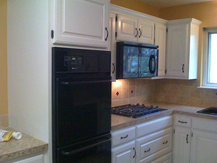 White kitchen cabinets with black oven and microwave, beige backsplash and countertops.