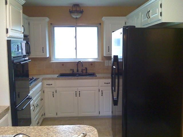 White kitchen with black appliances, white cabinets, and a window.