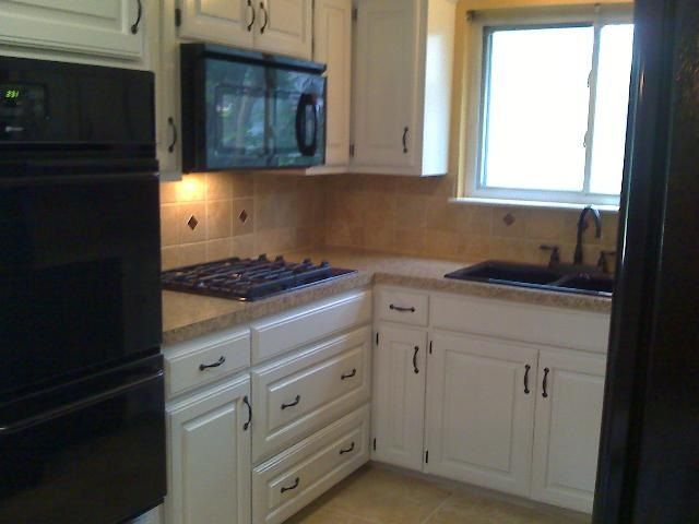 White kitchen cabinets with black appliances, microwave, and sink, next to a window.