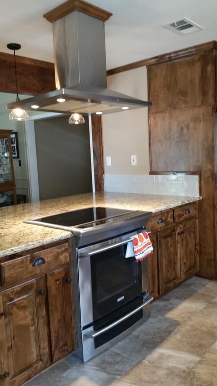 Kitchen with stainless steel oven, cooktop, and range hood. Wooden cabinets and light countertops.