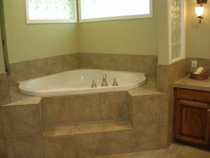 Corner bathtub with tiled surround and step. Beige tiles and light green walls.