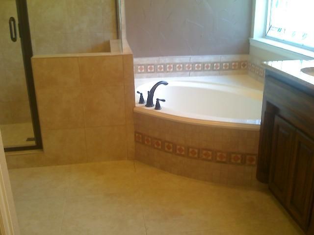 Bathroom with a tiled floor and walls, a tub with decorative tiles, and a dark-colored faucet.