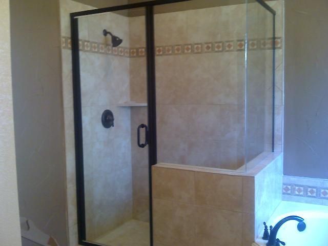 Shower enclosure with black trim, glass panels, and beige tile walls.