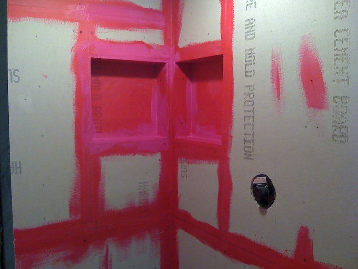 Shower area with red waterproof sealant applied to cement board walls, including built-in shelves.