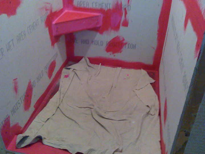 Shower stall with pink waterproofing; beige shirt on floor.