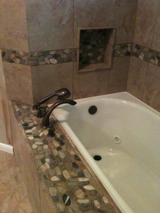 Bathroom with a white bathtub, dark faucet, and stone tile accents.