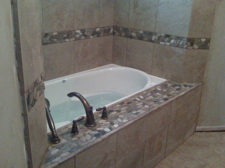 Built-in bathtub with stone tile surround and decorative stone border.