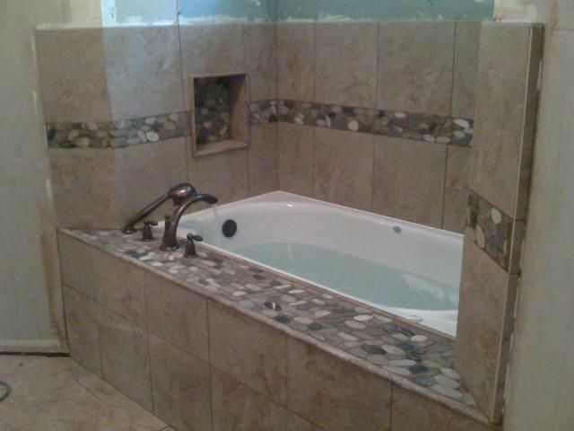 Tiled bathroom with a bathtub, stone border, and a built-in shelf.