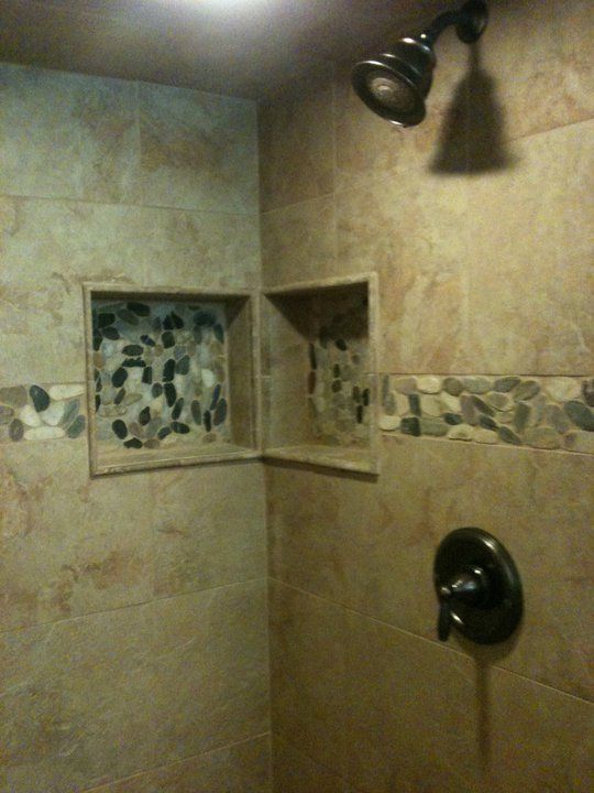 Shower with beige tiles, pebble accents, and recessed shelves.