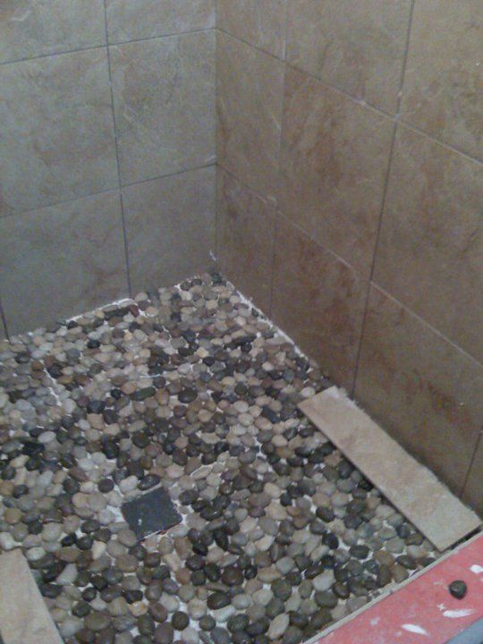 Shower stall with pebble tile floor and beige wall tiles.