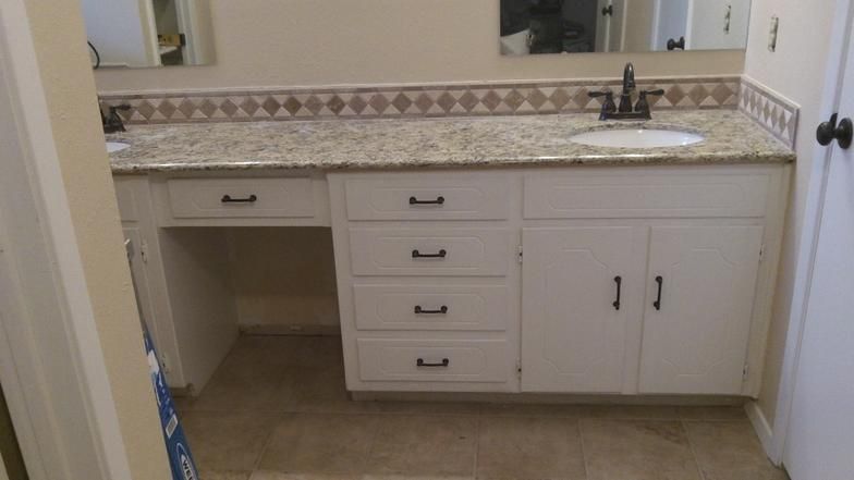 White bathroom vanity with granite countertop, dark hardware, and decorative tile.