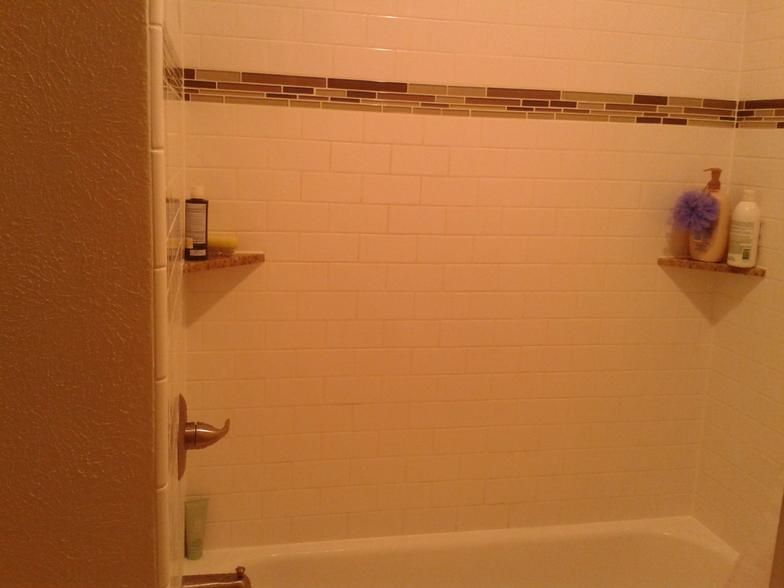 White tiled shower with brown accent tile, small shelves holding toiletries.