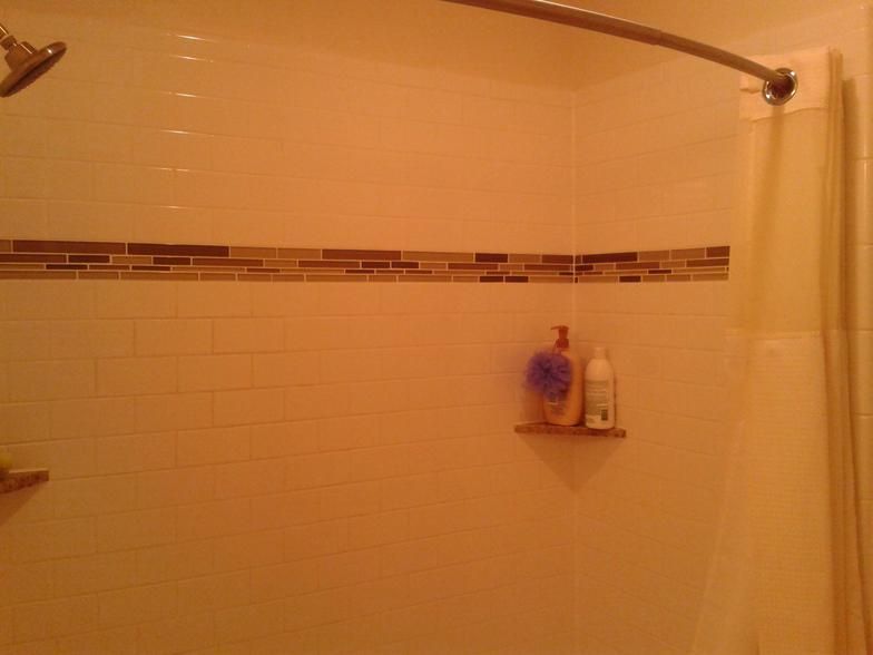 Shower with beige tile, glass tile accent, soap bottles on shelf, shower curtain, and curved rod.
