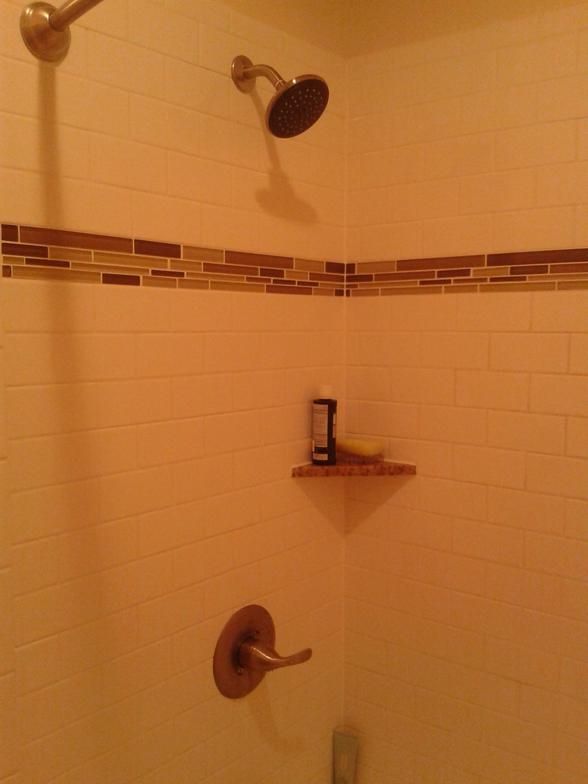 Shower stall with brown and beige tile, showerhead, and a corner shelf with product.