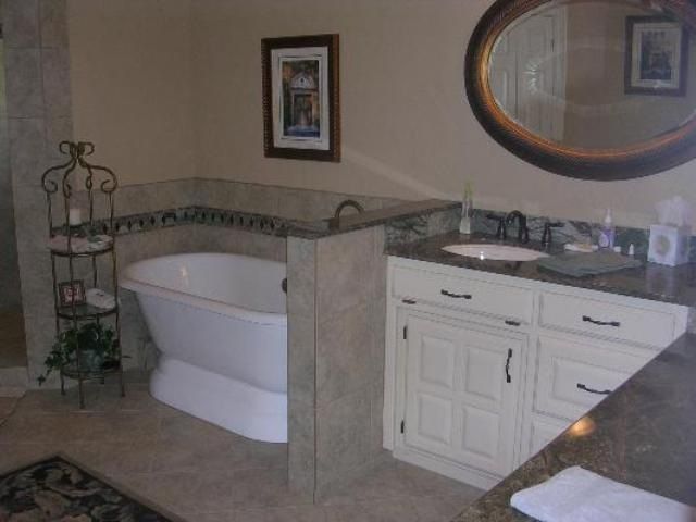 Bathroom with a white freestanding tub, vanity with a brown countertop, and an oval mirror.