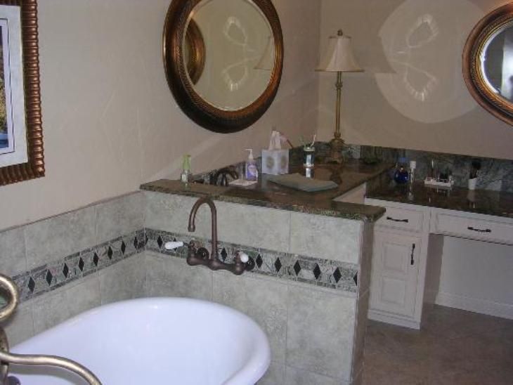 Bathroom with tub and vanity; cream and brown tones, marble countertop, round mirrors.