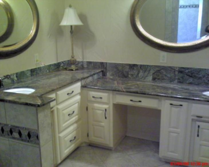 Bathroom vanity with two sinks, two mirrors, and cream-colored cabinets. Granite countertop, a desk area, and a lamp.
