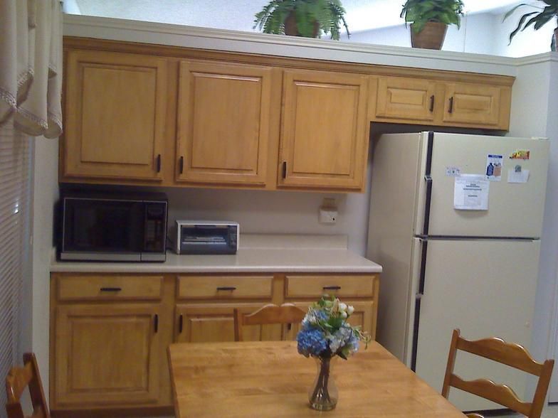 Kitchen with light wood cabinets, countertop, microwave, refrigerator, and table with flowers.