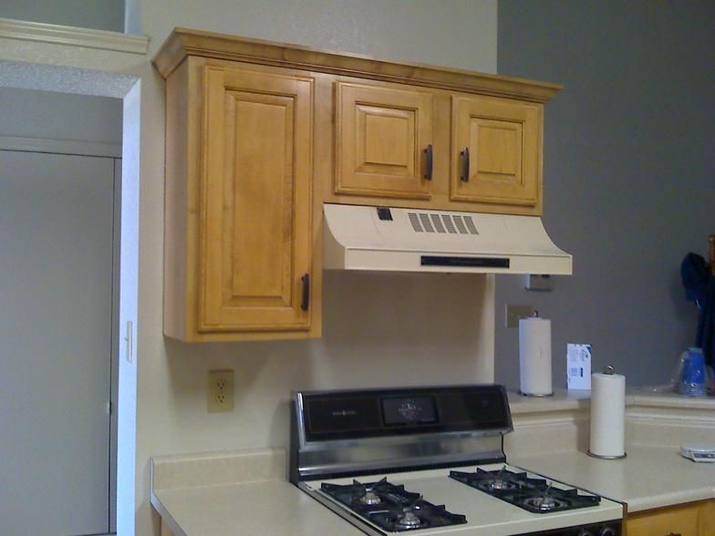 Kitchen with light-colored cabinets, stove, and range hood. Cream-colored walls.