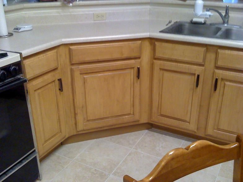 Corner kitchen cabinets with light wood doors, beige countertop, and a black stove.