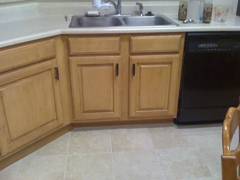 Kitchen corner with wood cabinets, stainless steel sink, black dishwasher, and tiled floor.