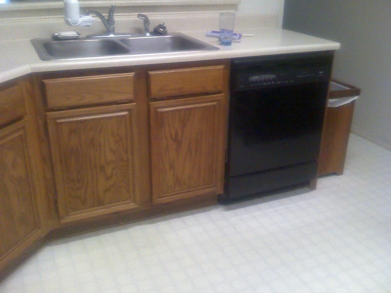Kitchen with oak cabinets, stainless steel sink, black dishwasher, and white countertop.