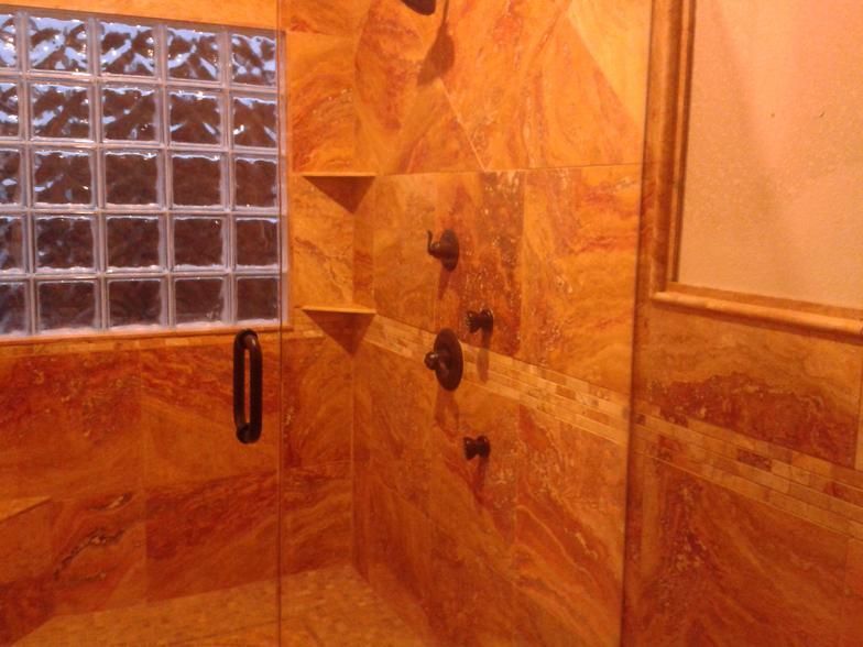 Orange-tiled shower with glass block window, dark fixtures, and built-in shelves.