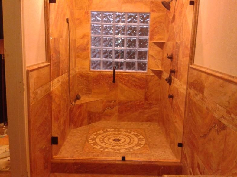 A tiled shower with a glass block window and a decorative floor.