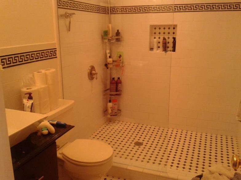 Bathroom with white tiled walls, black and white tiled floor, toilet, shower, and shelves with toiletries.