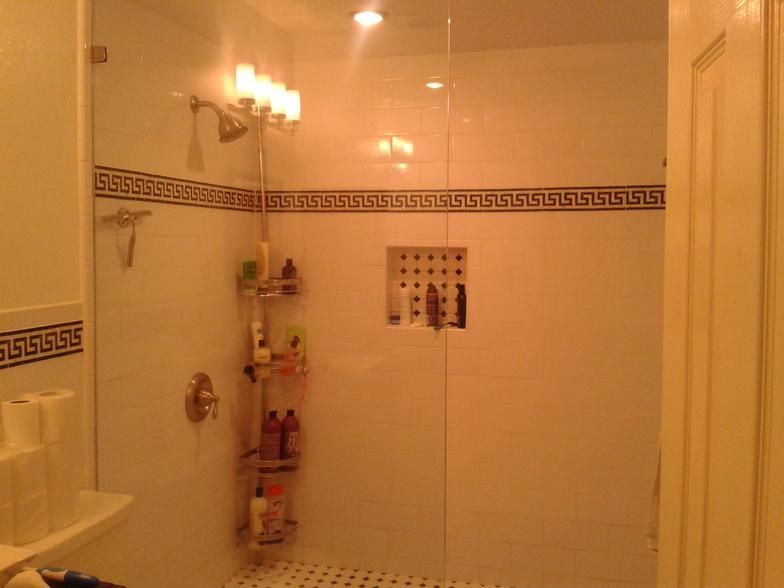 A shower with white tile, gold fixtures, and a Greek key border.