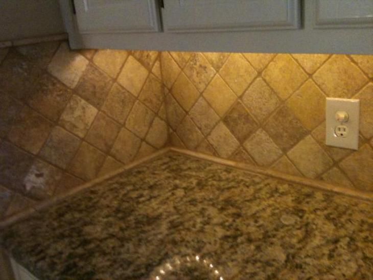 Kitchen counter with granite surface, diamond-patterned tile backsplash, and outlet.