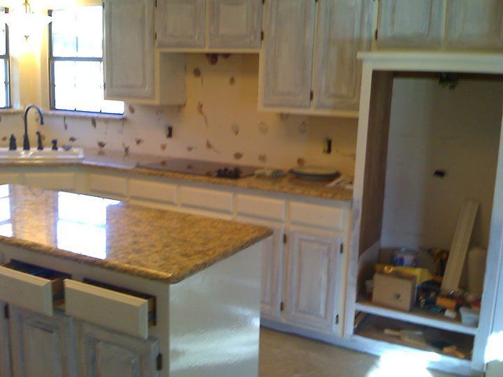 Kitchen renovation, white cabinets, granite countertops, island with drawers open, unfinished appliance space.