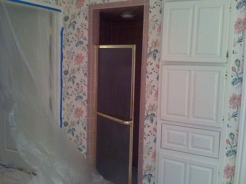 Bathroom with floral wallpaper, white cabinets, and a shower door. Plastic sheeting covers part of the scene.
