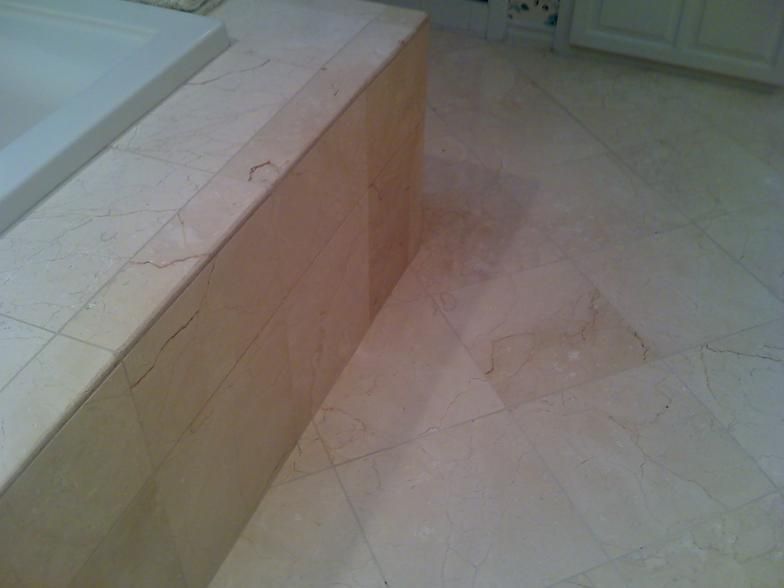 Cream-colored marble bathroom floor and tub surround. Diagonal tiles create an irregular pattern.