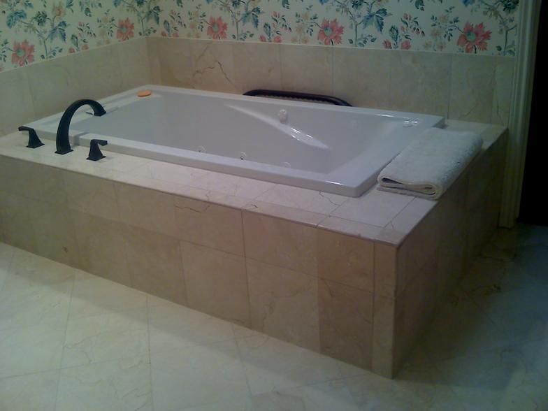A rectangular bathtub built into a stone-tiled platform; faucet and controls are black.