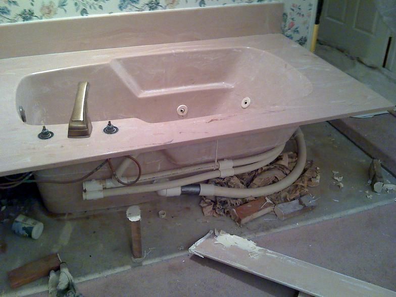 A built-in beige bathtub in a bathroom during renovation, with exposed pipes and debris on the floor.