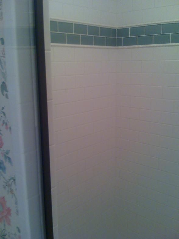 White tile shower wall with a horizontal band of blue tiles.