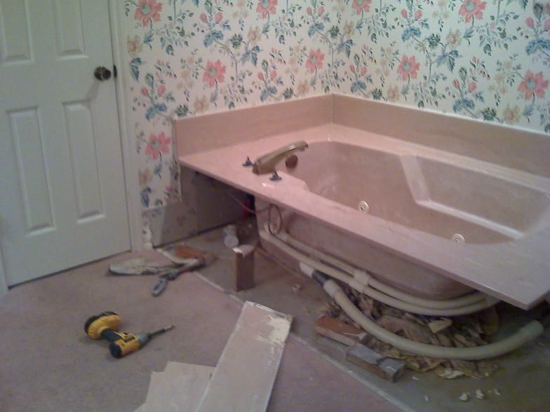 Bathroom renovation: Tub with exposed plumbing, tools on floor, floral wallpaper.