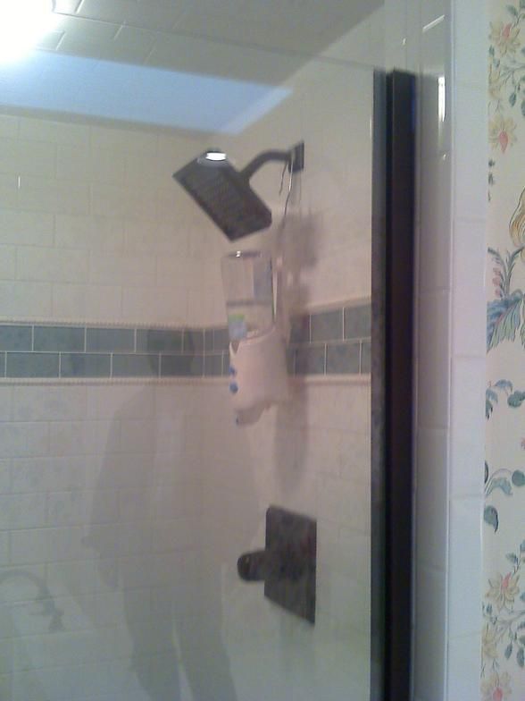 Shower with glass door, square showerhead, dark fixtures, and white and teal tiled walls.