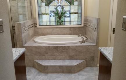 Bathroom with built-in bathtub, tile surround, and stained glass window above. Two vanities on each side.