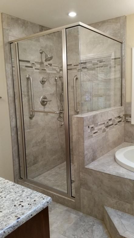 Glass-enclosed shower in a tiled bathroom, with grab bars, and a step-up platform for a bathtub.