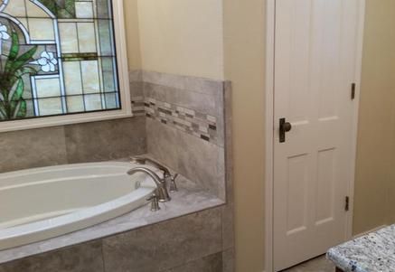 Bathroom with a built-in tub, tiled surround, stained glass window, and a closed white door.