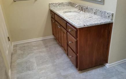 Bathroom vanity with granite countertop and wooden cabinets; gray tiled floor.