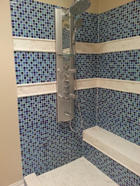 Blue tiled shower with a silver shower panel and marble shelves.