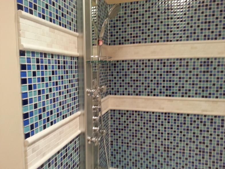 Blue and white tiled shower with stainless steel fixtures and decorative white bands.