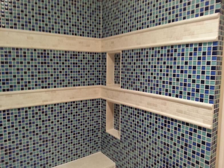 Blue tiled shower with built-in shelves. Off-white trim against the blue and square tiles.